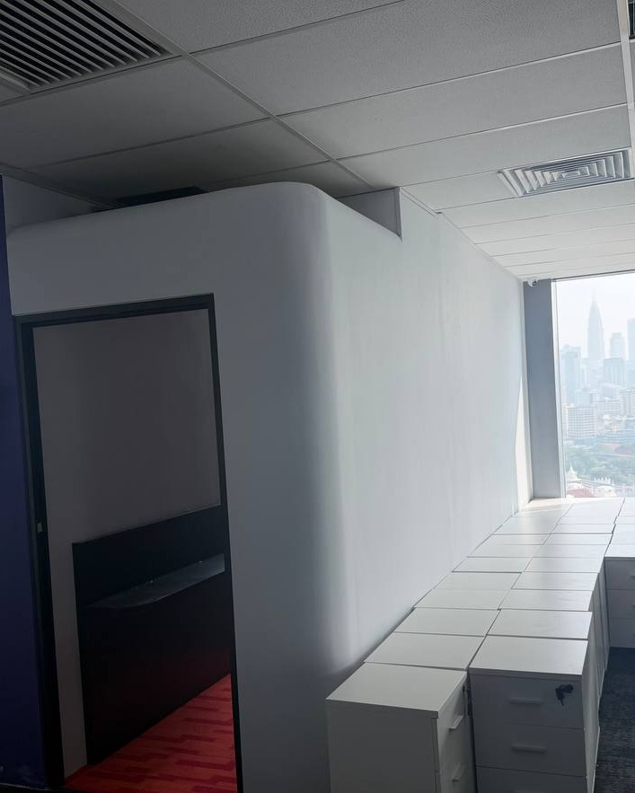 Rounded Plaster Partition Wall - Brickfields Office Curved white plaster partition wall with rounded corner beneath a suspended grid ceiling in Brickfields office, overlooking Kuala Lumpur skyline through window