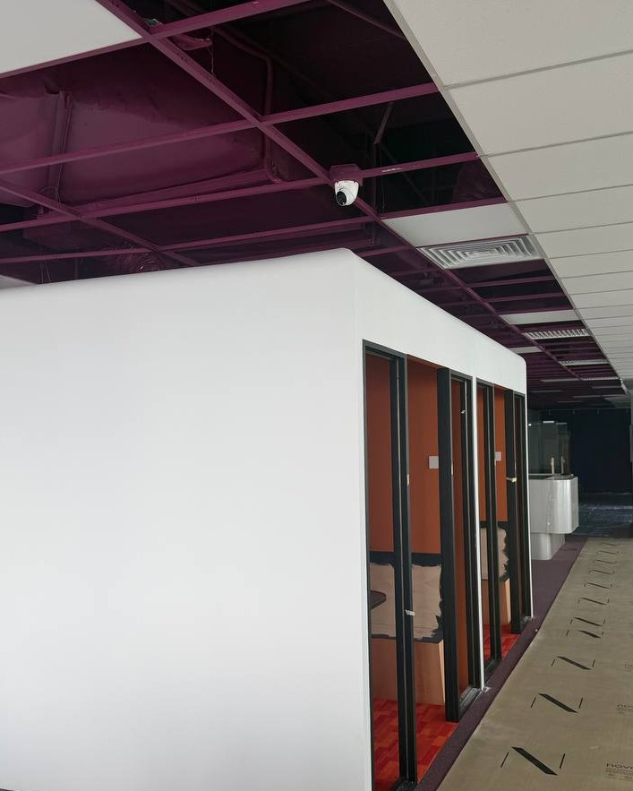Partition Wall Corner & Exposed Ceiling Grid – Brickfields White partition wall corner with glass-panelled office pods and exposed purple ceiling structure at Brickfields office renovation