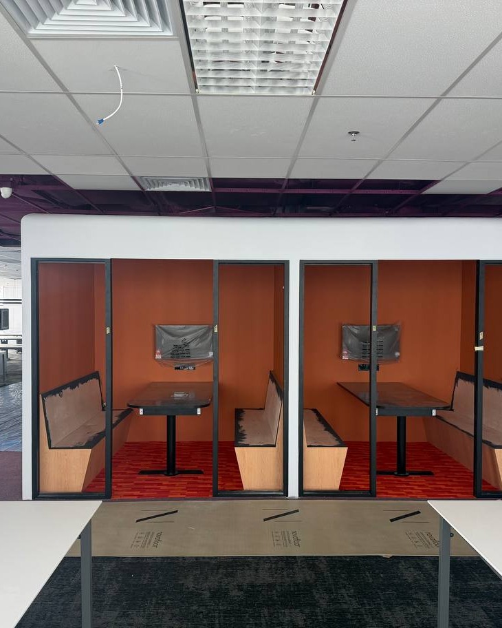 Meeting Booth Partitions – Brickfields Office Suspended grid ceiling above glass-partitioned meeting booths featuring orange feature walls and built-in banquette seating, Brickfields office fit-out
