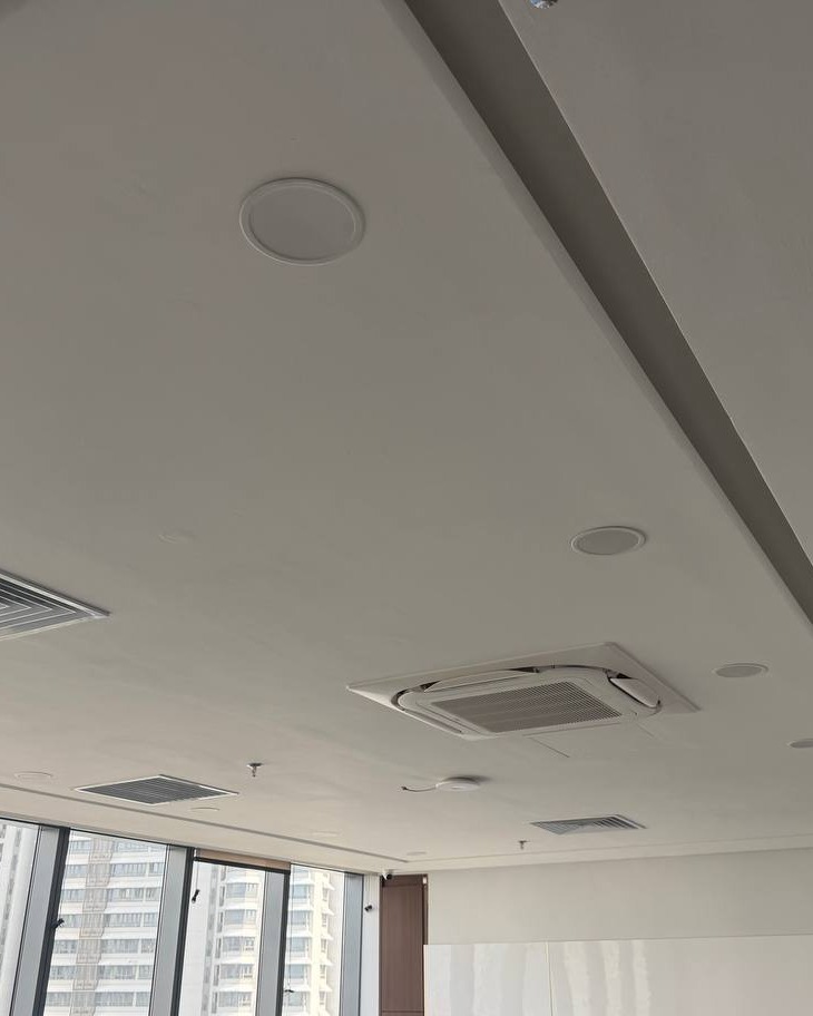 Plaster Ceiling with Cassette AC and Speaker Fittings – Brickfields Office White plaster ceiling in Brickfields office with recessed downlight trims, ceiling speakers, and built-in cassette air conditioning unit alongside a stepped bulkhead detail