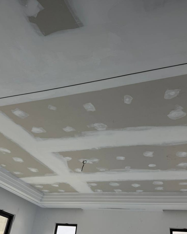 Plaster Ceiling Drop Panel Mid-Construction, Cyberjaya Unfinished plaster ceiling with joint compound patches and taped seams, recessed drop panel and cove lighting ledge under construction, Cyberjaya residential staircase project