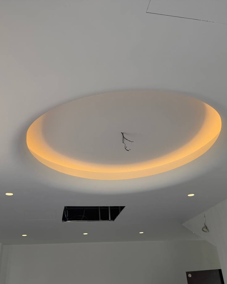 Circular Light Trough Plaster Ceiling - Klang Oval plaster ceiling drop with recessed cove lighting trough glowing warm amber, Klang residence false ceiling installation mid-wiring stage