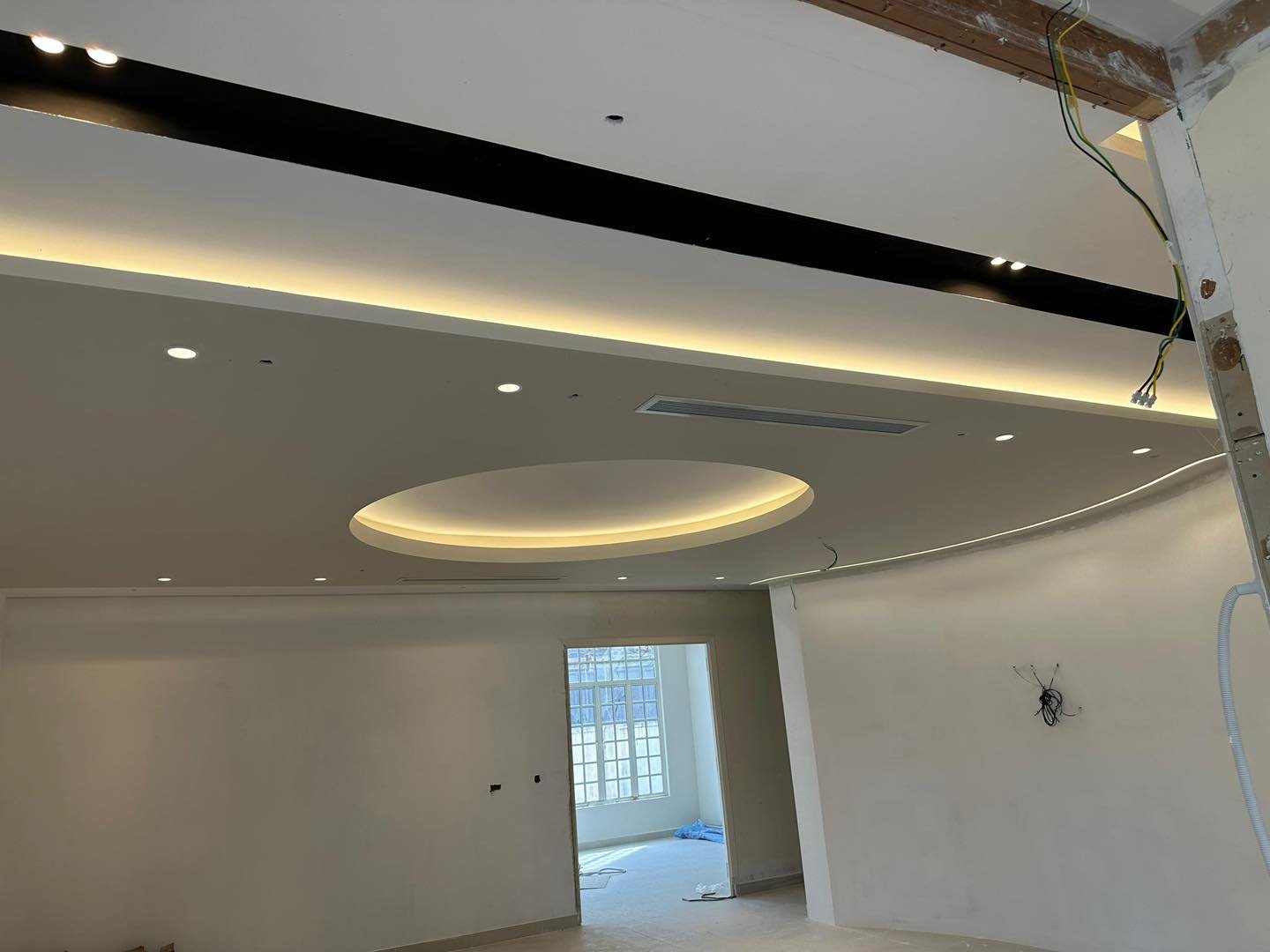 Circular Floating Moon Ceiling Centrepiece - KL Bungalow Circular recessed plaster ceiling centrepiece with warm cove lighting above a curved partition wall edge, black accent ceiling band and aircon vent, Kuala Lumpur bungalow renovation