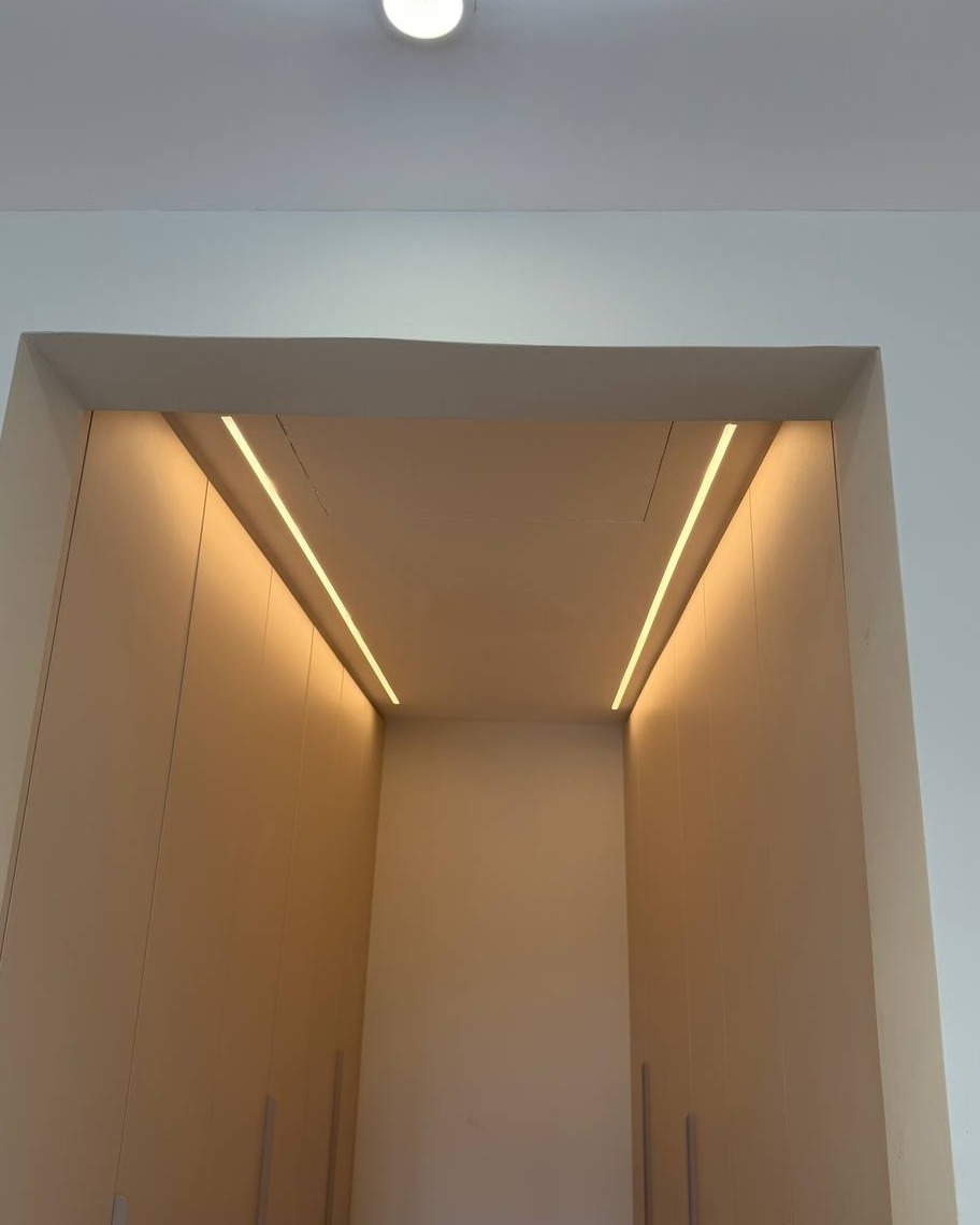 Wardrobe Alcove LED Strip Lighting Detail, Rawang View looking up into a wardrobe alcove in Rawang with plaster ceiling recess and two parallel warm-toned LED strip lights running along the sloped ceiling edges above built-in cabinet doors