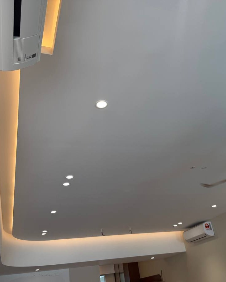 Curved Plaster Ceiling with Cove Lighting - Rawang Home Curved plaster ceiling with cove lighting and recessed LED downlights in Rawang residential ground floor, showing indirect warm light strip along the drop-down border and split unit air conditioner fitted into the design