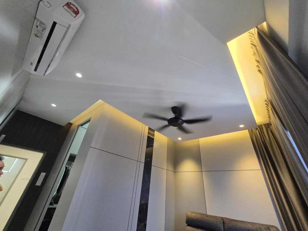 Customized plaster ceiling in a KL bedroom, enhanced with warm ambient cove lighting and ceiling fan for a cozy modern interior.