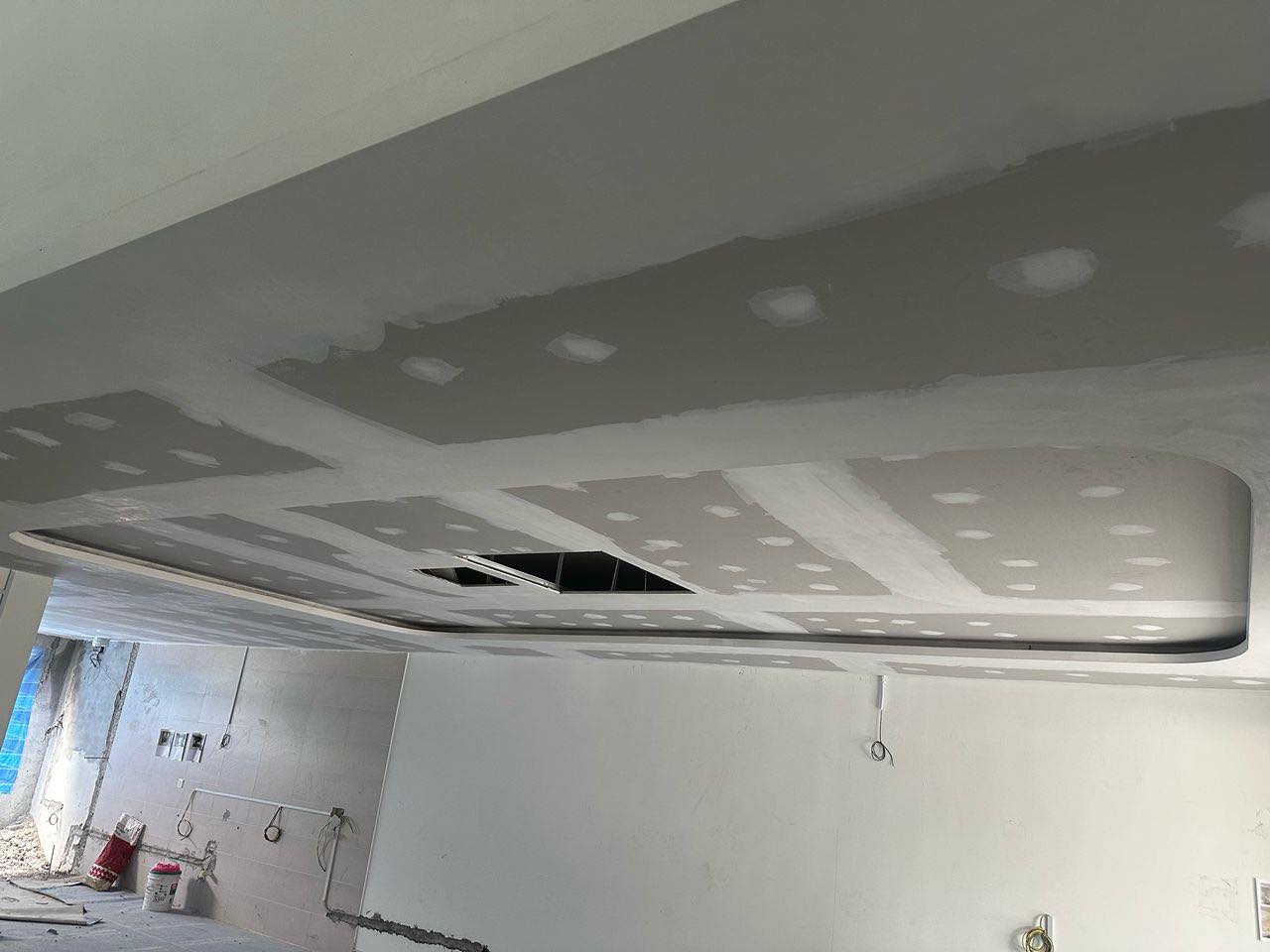 Ceiling construction featuring a curved recessed bulkhead. Joint lines and screw holes are patched, indicating progress before final finishing. Wiring and surface work are still underway.