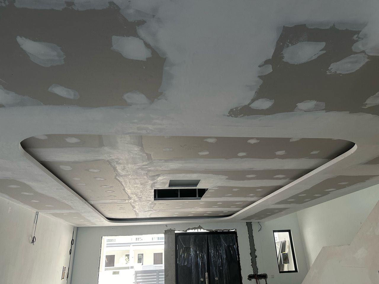 A rounded plaster ceiling centerpiece under construction, showing visible joint compound patching and an access opening. Designed to enhance room aesthetics with soft curves and future lighting integration.