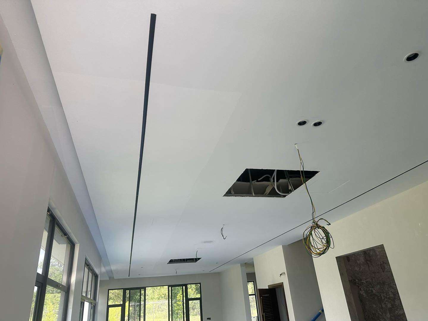 Work-in-progress plaster ceiling featuring a sleek linear groove, spotlight fittings, and wiring access points. Natural light fills the room, highlighting the modern layout.