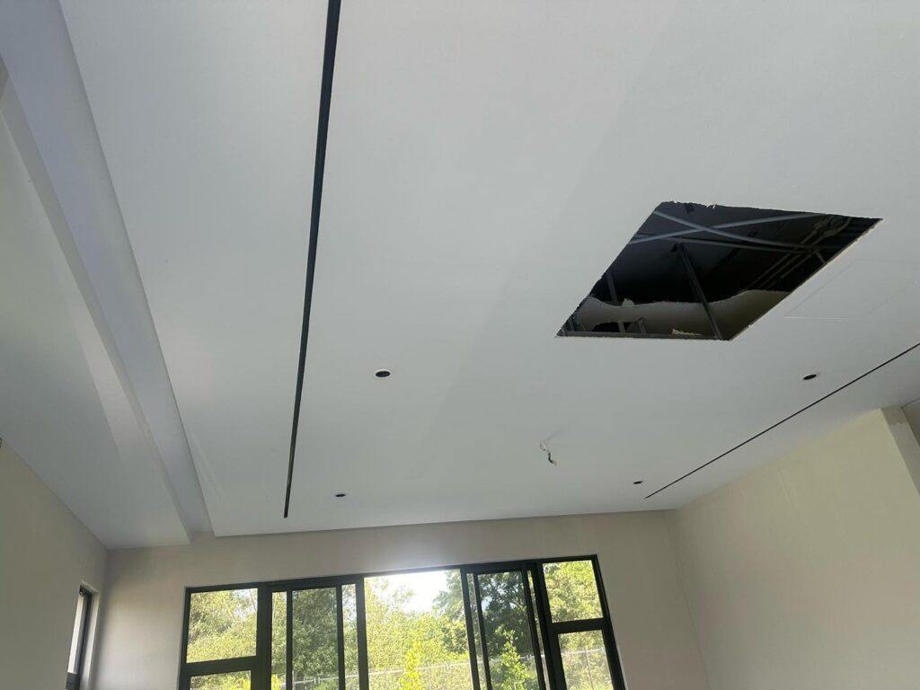 Plaster ceiling work in progress: Featuring elegant linear groove design, recessed spotlight points, and ceiling panel access for utility. Natural light enhances the contemporary finish.