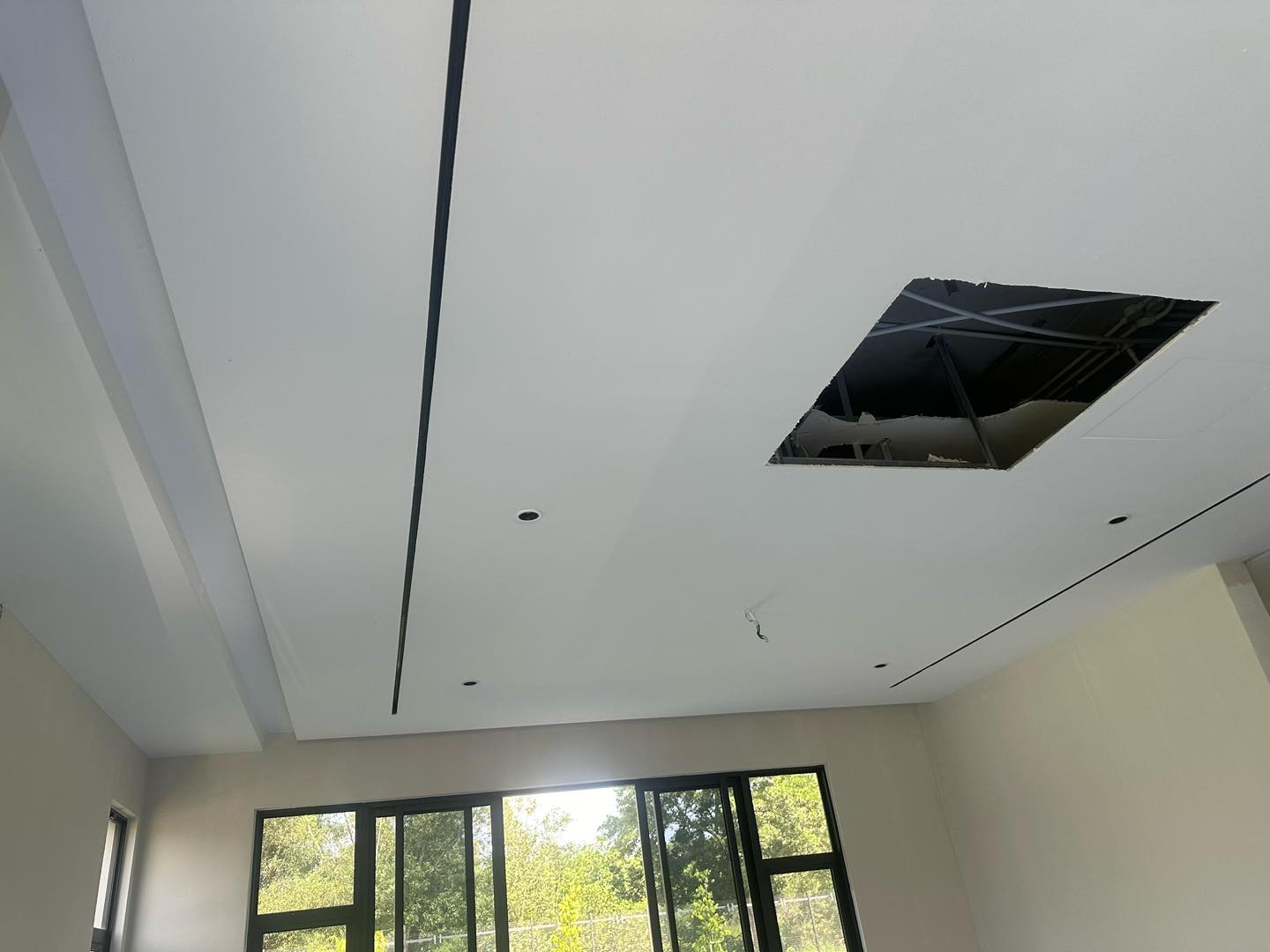 Plaster ceiling work in progress: Featuring elegant linear groove design, recessed spotlight points, and ceiling panel access for utility. Natural light enhances the contemporary finish.