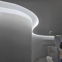 A sleek modern design featuring a curved gypsum wall blending seamlessly into the plaster ceiling, accentuated by soft recessed LED cove lighting.
