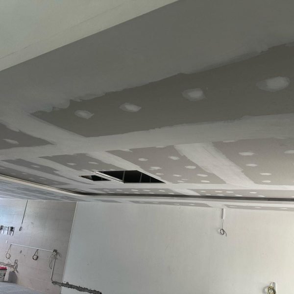 Ceiling construction featuring a curved recessed bulkhead. Joint lines and screw holes are patched, indicating progress before final finishing. Wiring and surface work are still underway.