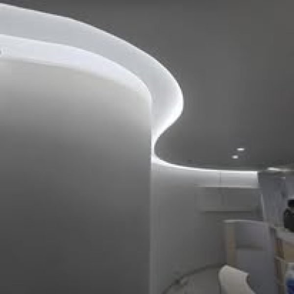A sleek modern design featuring a curved gypsum wall blending seamlessly into the plaster ceiling, accentuated by soft recessed LED cove lighting.
