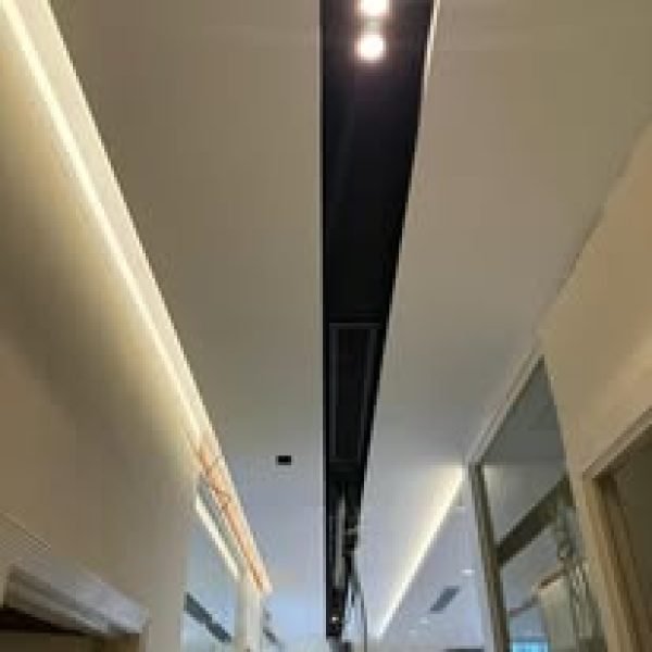 A modern plaster ceiling design in an office hallway, showcasing clean recessed lights and a centralized ventilation slot for sleek functionality.
